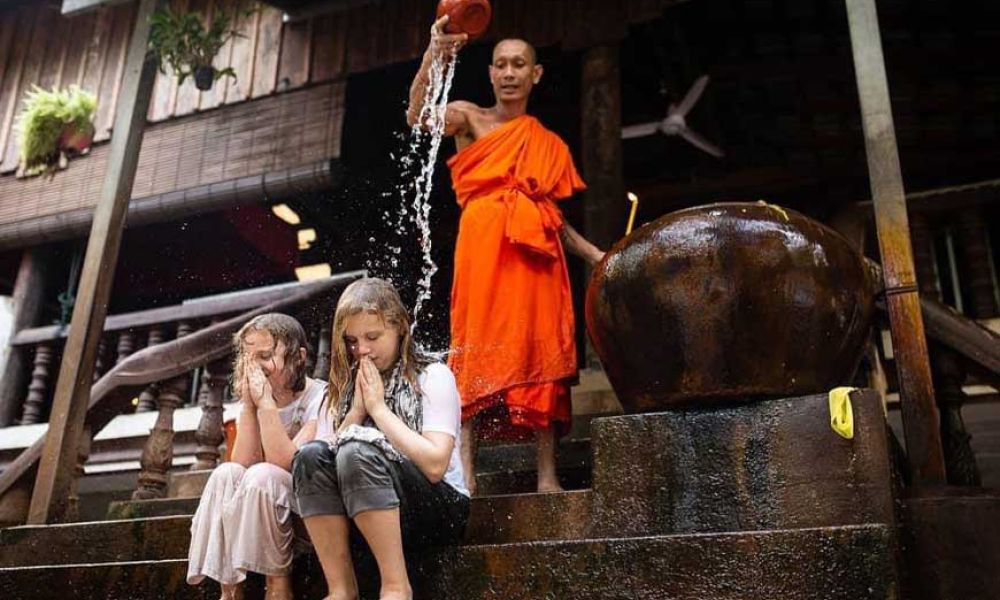 A Buddhist monk performing a traditional Cambodian water blessing for two young female guests.