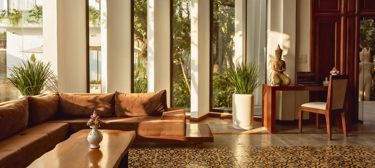 A bright, sunlit lobby lounge at Shintana Saya Residence in Siem Reap, featuring plush brown sofas, tall windows, and Khmer-inspired decor.